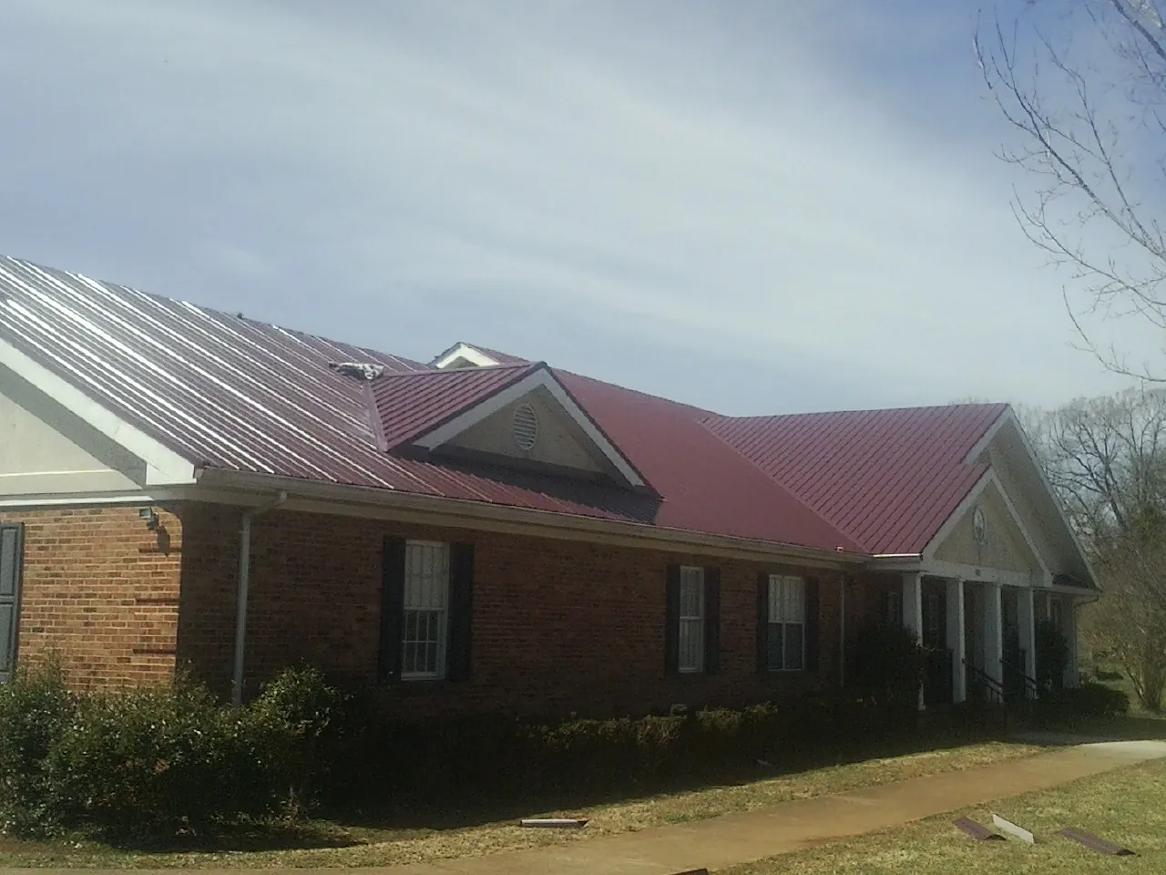 Red metal roof with gabled entries on a long brick building, from a Hail Damage Roof Repair job in Fulton